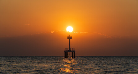 Wall Mural - sunset sky over silhouette lighthouse tower on the sea in the evening