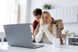 © LIGHTFIELD STUDIOS - laptop and cup on desk near caring boyfriend in sweater covering freezing blonde girlfriend with blanket.