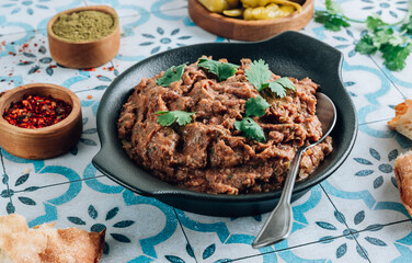 Wall Mural - Mashed red bean with spices on blue tiles background. Traditional georgian dish lobio in black plate with bread and pickled hot peppers.