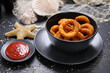 Panko squid rings served with tomato sauce, ketchup. Deep fried calamari in a black bowl, on a table, selective focus.