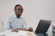 © VK Studio - Smiling african american man working on laptop on business project, reading email with good news