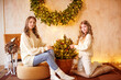 Lovely girls with blonde curly hair  in   a white knitted sweaters and blue jeans next to a large Christmas wreath of pine needles on the wall  in a classic interior. Christmas mood 