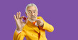 Portrait of crazy goofy bearded adult man in funky yellow suit on purple studio background pointing at poker chip and looking at it with funny angry face expression. Casino, gambling addiction concept