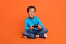 Full Length Photo Of Adorable Little Boy Hold Joystick Playstation Enjoy Weekend Wear Trendy Blue Look Isolated On Orange Color Background