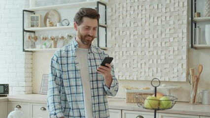 Portrait of a handsome bearded middle-aged man texting on the phone in his kitchen. Close-up of a smiling man's face. Pleasant communication with friends online, creating a post in a social network