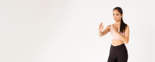 Sport, wellbeing and active lifestyle concept. Serious-looking asian girl going to self-defense classes, standing in fighting, martial arts pose, wearing activewear for workout, white background