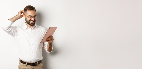 Wall Mural - Confused male manager looking puzzled at digital tablet, scratching head doubtful, standing over white background