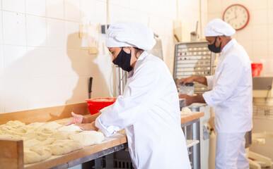 Wall Mural - Latin american female baker engaged in breadmaking, forming bread loaves from raw dough