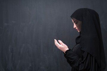 Portrait of beautiful muslim woman in fashionable dress with hijab making traditional prayer to God keeps hands in praying gesture isolated on black background