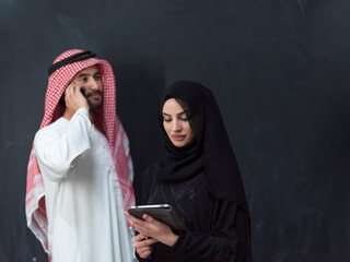 Wall Mural - Young muslim business couple in fashionable hijab dress using smartphone and tablet in front of black background