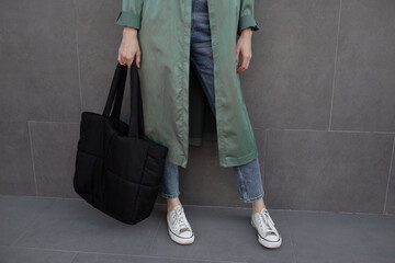 Wall Mural - A beautiful girl is wearing a grey t-shirt, cloth cap, coat, black bag and jeans posing against the background of a wall. fashion outfit for the city, minimalism urban style clothing