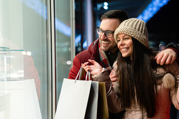 Cheerful happy couple doing Christmas shopping standing on decorated street. Sale people concept