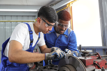 Multiethnic technicain mechanic or worker man in protective uniform using metal lathe machine operate polishing car disc brake at garage. Maintenance automotive and inspecting vehicle part concept