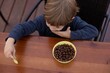 © Татьяна Волкова - Little boy sitting on chair at brown wooden table in kitchen and having breakfast with chocolate balls top view. Kid of kindergarten age trifle spoon in hand. Ready breakfast, not hungry child