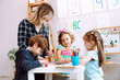 © Татьяна Волкова - Group of kids playing together with educational toys in playroom of kindergarten. Young educator sitting with children at table on floor and help to play learning games. Lesson in daycare centre