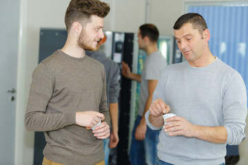 two men chatting holding disposable cups from vending machine