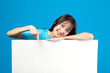 © ueaphan - Portrait of smiling asian woman holding empty blank board on blue studio background. Happy young girl standing with white square paper card for text and showing card to camera.