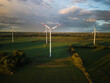 Aerial view of wind turbines under a cloud sky during sunset with long shadows