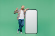 Full body young blond man with dreadlocks in casual shirt big huge blank screen mobile cell phone with workspace copy space mockup area point finger up isolated on pastel plain light green background.