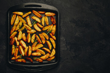 Wall Mural - Roasted potatoes. Baked potato wedges in frying tray on dark stone background. Top view with copy space.