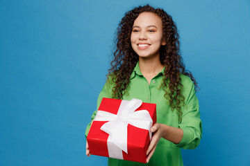 Wall Mural - Young woman of African American ethnicity 20s she wear green shirt hold in hand give red present box with gift ribbon bow isolated on plain blue background studio portrait. People lifestyle concept.