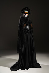 Wall Mural - full length of woman in spooky costume and mexican day of dead makeup standing on black background.