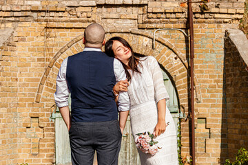  beautiful girl in a white dress and a guy on the background of a brick wall with an old gate