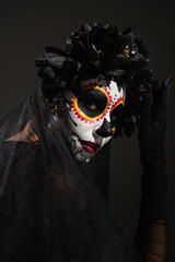 Wall Mural - portrait of woman in sugar skull halloween makeup and dark wreath with veil looking at camera isolated on black.