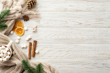 Winter mood concept. Top view photo of pine cone spruce branches cup of cocoa with marshmallow knitted plaid dried orange slices anise cinnamon sticks on white wooden desk background with copyspace