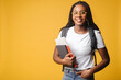 © Vadim Pastuh - Inspired multiracial female student in white t-shirt and jeans with backpack isolated on yellow, foreigner woman in glasses proud to be university member, looking at the camera standing indoors