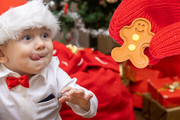 Wall Mural - Little boy with a Santa Claus hat looks at gingerbread figurine in a hand