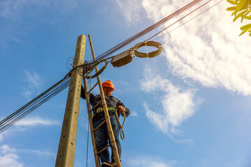 Wall Mural - A telecoms worker is shown working from a utility pole ladder while wearing high visibility personal safety clothing, PPE, and a hard hat..