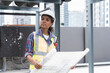 © amorn - Female engineer working with construction building blueprint at sewer pipes area at construction site on rooftop of building