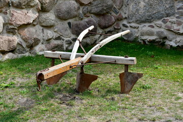 A close up on an old ploughing machine used by peasants and farmers many years ago with proper handles, curved frame and metal elements seen on a well maintained lawn in Poland in summer