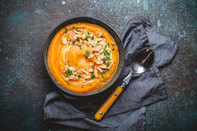 A Ceramic Bowl With Pumpkin Cream Soup Decorated With Peanuts On Dark Stone Background With Spoon Decorated, From Above. Autumn Cozy Dinner Concept 
