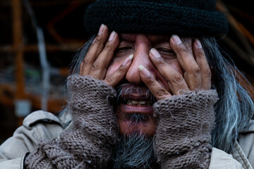 Wall Mural - Close-up of the face of a dirty-dressed, long-haired, homeless old man with his hands covering his face. which shows signs of severe stress, no food to eat and no work to sleep in the streets.