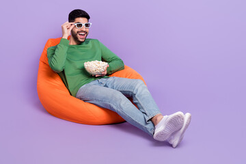 Full size photo of young excited hispanic man watching movie eat popcorn dressed trendy green outfit isolated on violet color background