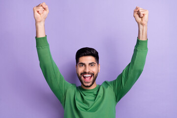 Wall Mural - Photo of astonished handsome positive stylish guy dressed green pullover raising fists up screaming isolated on violet color background