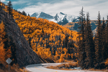 an asphalt road winds though the colorado rocky mountains during fall with winter snow capped mounta