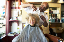Barber Cutting Cute Little Boy's Hair At Barbershop