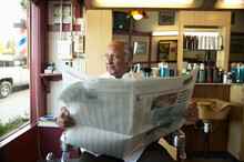 Senior Black Businessman Owner In Barber Shop With Newspaper