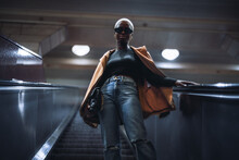 A Stylish Young Black Female In A Coat And With A Clutch Is Descending Using An Escalator; A Fashionable Very Short-haired African Woman On The Moving Staircase Of The Metro Or An Underground Passage