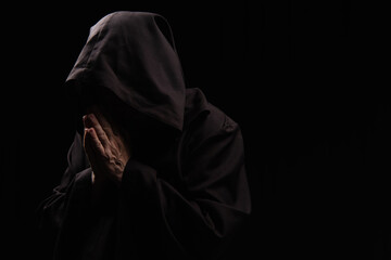 Poster - mysterious priest in hooded robe praying isolated on black.