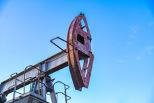 An Abandoned Oil Or Gas Rocking Machine Against A Blue Sky, Exhausted Resource. A Clogged Field Of Gas And Oil Production.
