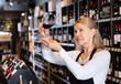 Confident mature female winemaker holding glass of wine, checking it in wine store..