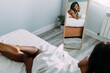 © David Prado/Stocksy - Black woman reflecting in mirror while lying on bed