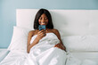 © David Prado/Stocksy - black woman using smartphone in bed