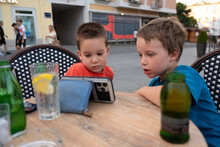 Two Boys Are Watching A Cartoon On A Phone In A Restaurant 