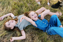 Two Sisters Laughing Together Lying Down In Grass