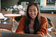 © Jovo Jovanovic/Stocksy - Happy Asian woman smiling at laptop while working in cafe